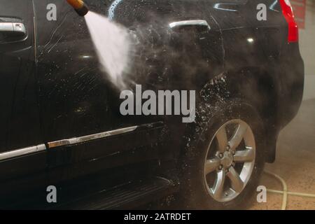 Un employé du lavage de voiture se lave soigneusement effectue le décollement et applique un équipement de protection au corps d'une voiture chère Banque D'Images