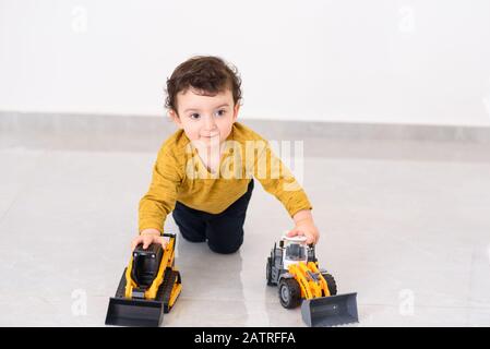 Petit garçon joue avec des voitures de jouet. Joyeux enfant jouant avec le jouet de voiture de tracteur à la maison. Banque D'Images