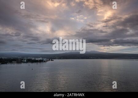 Hilo, Hawaï, États-Unis. - 14 janvier 2020: Spectaculaire paysage de nuit plus clair avec des taches de lumière du soleil jaune sur la ville et le volcan à l'horizon. Banque D'Images