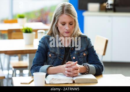 Une femme mûre priant, après avoir fait une étude biblique personnelle, dans un café; Edmonton, Alberta, Canada Banque D'Images