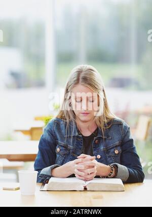 Une femme mûre priant, après avoir fait une étude biblique personnelle, dans un café : Edmonton, Alberta, Canada Banque D'Images