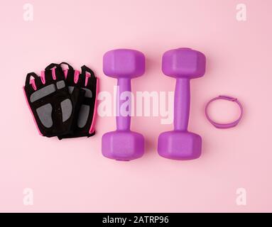 paire de haltères en plastique violet et de gants noirs sur fond rose, équipement d'entraînement, vue de dessus Banque D'Images
