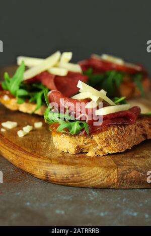 Concept de la cuisine italienne. Bruschetta avec prosciutto, fromage pecorino, salade de roquettes et confiture de figues sur table en bois. Banque D'Images