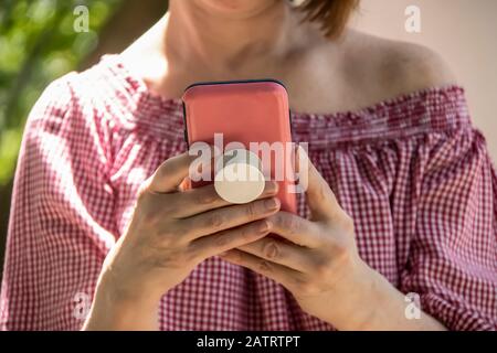 Gros plan d'une femme tenant et lisant à partir d'un téléphone portable dans un étui rose avec poignée sur le dos - hors de l'épaule chemisier et les cheveux courts - mise au point sélective Banque D'Images