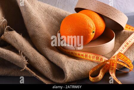 Fruits orange de couleur juteuse sur fond de tissu beige. Oranges dans une boîte en bois rond ECO attaché avec un noeud de ruban de mesure jaune. Concept de nourriture biologique saine. Fruits placés dans l'emballage sur un tissu en toile de rackCloth. Banque D'Images