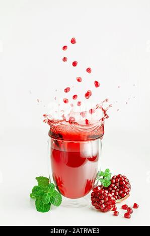 Graines de grenade survolant les projections de jus dans un verre. Concept de mode de vie sain. Banque D'Images