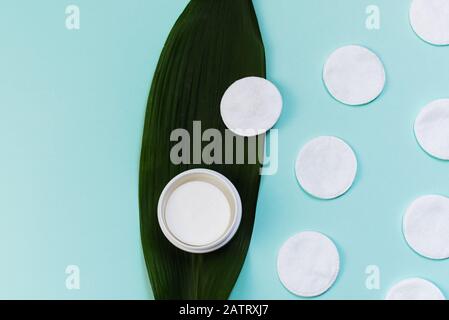 Bol avec tampons en coton liquide pour nettoyer la peau sur une feuille de palmier. Nettoyage des tampons en coton sur fond bleu pastel. CopySpace, planéité. Banque D'Images