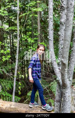 Une pré-adolescente balance tout en marchant sur une bûche dans une forêt; Salmon Arm, Colombie-Britannique, Canada Banque D'Images