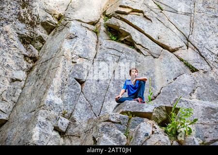 Boy est assis sur une corniche de roche qui regarde avec une expression sérieuse; Colombie-Britannique, Canada Banque D'Images