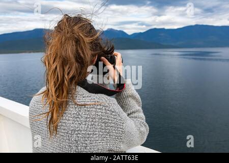 Photographe de jeune femme tourné de derrière tout en prenant des photos du pont d'un ferry. Équipement photographique coûteux et téléobjectif long. Banque D'Images