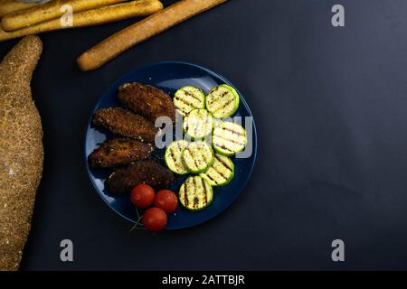 Ailes de poulet frit dans la pâte, avec courgettes grillées et tomates sur la plaque bleue. Banque D'Images