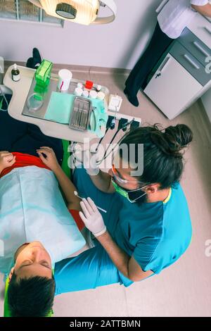 Un jeune garçon de patient est assis dans une chaise de dentiste et un dentiste de sexe masculin examine ses dents Banque D'Images