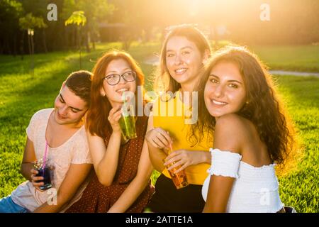 Jeunes et jolis amis avec des cocktails le jour ensoleillé de l'été dans le parc ayant de bons moments. Portrait demi-longueur style de vie de groupe. Banque D'Images