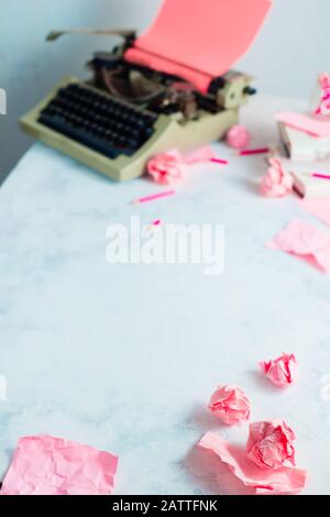 Boules de papier roses froissés et machine à écrire sur un lieu de travail d'écrivain. Profession créative féminine. Banque D'Images