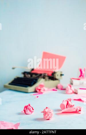 Boules de papier roses froissés et machine à écrire sur un lieu de travail d'écrivain. Profession créative féminine. Banque D'Images