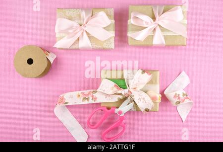 Cadeaux enveloppés dans du papier kraft et ruban rose frais généraux mise à plat pour la Fête des Mères, un anniversaire ou la Saint-Valentin célébrations. Banque D'Images