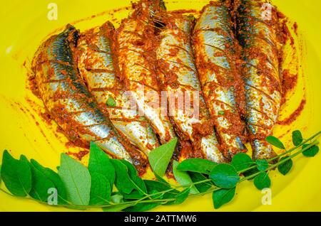 Sardines marinées avec le masala de Chili prêt à frire garnies de feuilles de curry dans une assiette jaune. Banque D'Images