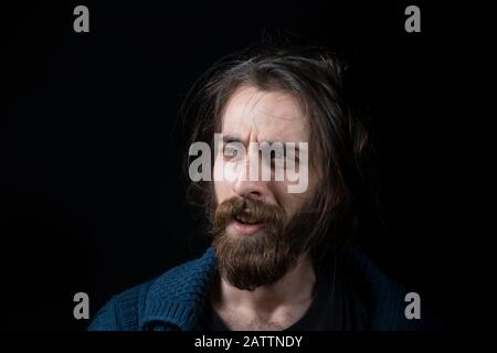 Jeune homme avec de longs cheveux avec barbe longue de type hippie, visage surpris, dans fond noir isolé. Concept Hipster. Banque D'Images