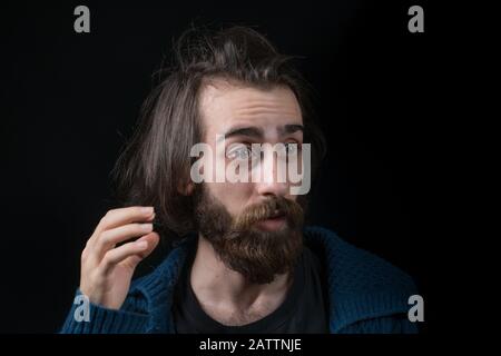 Jeune homme avec de longs cheveux avec barbe longue de type hippie, visage surpris, dans fond noir isolé. Concept Hipster. Banque D'Images