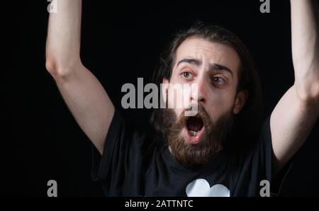 Jeune homme avec de longs cheveux avec barbe longue de type hippie, visage surpris, dans fond noir isolé. Concept Hipster. Banque D'Images