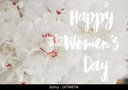Happy Women's Day texte manuscrit sur beau bouquet de pivoine gros plan sur fond de mur blanc. Pivoines blanches élégantes avec pétales rouges. 8 mars Banque D'Images