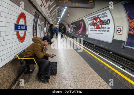 Un homme est assis sur un banc et utilise son téléphone mobile lorsqu'il attend un train à la station de métro St Paul de Londres. Banque D'Images