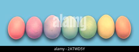 Oeufs de Pâques peints en pastel alignés sur fond bleu panoramique, bannière de Pâques Banque D'Images