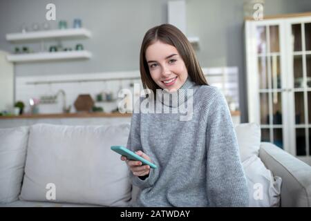 Fille aux cheveux sombres dans un pull gris souriant avec bonheur Banque D'Images