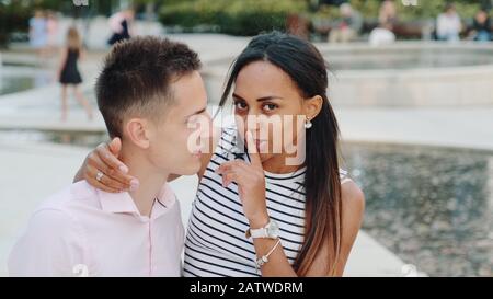 Gros plan sur une femme de race mixte chuchotant quelque chose dans l'oreille de mon ami et montrant garder le silence geste à l'appareil photo. Elle lui dit des choses spéciales. Banque D'Images