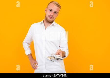 un homme blond dans une chemise blanche tient des paquets de billets d'argent en papier sur un fond jaune Banque D'Images
