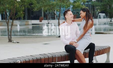 Jeune famille mixte ayant de beaux moments à l'extérieur: Rire, embrasser et parler les uns avec les autres. Les fontaines sont à l'arrière-plan. Banque D'Images