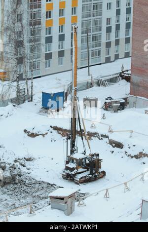 Un tracteur équipé d'un dispositif de conduite de pieux se trouve sur un chantier en hiver. Banque D'Images