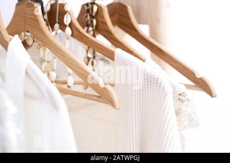 Détail de vêtements blancs accrochés sur des cintres en bois dans un magasin de mode. Banque D'Images