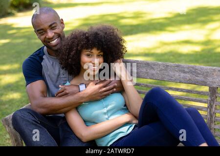 Un jeune couple heureux assis sur un banc dans le jardin Banque D'Images