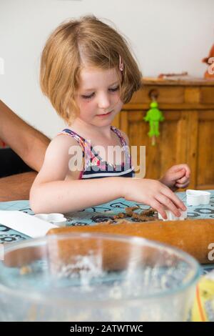 Fille de 5 / 5 ans utilisant un couteau à pâtisserie pendant la cuisson de la recette de biscuit à partir d'ingrédients / biscuits; la maison de cuisson des biscuit avec des enfants / enfants. (112) Banque D'Images