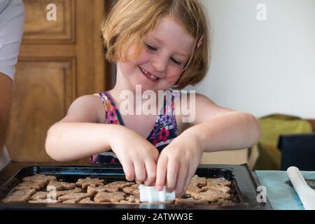 Fille de 5 / 5 ans utilisant un couteau à pâtisserie pendant la cuisson de la recette de biscuit à partir d'ingrédients / biscuits; la maison de cuisson des biscuit avec des enfants / enfants. (112) Banque D'Images