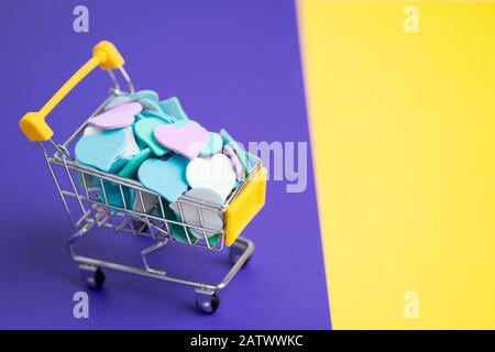 Gros plan d'un panier miniature plein de coeurs colorés sur un fond jaune et bleu à deux tons. Saint Valentin, printemps, amour, réductions et pr Banque D'Images