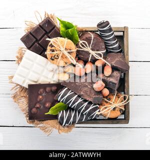 Un ensemble de chocolat au lait et de chocolat noir dans une boîte en bois avec des noix et des biscuits. Sur un fond en bois blanc. Espace de copie pour le texte. Banque D'Images