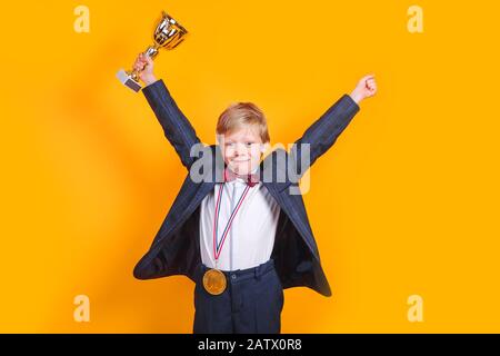 Un jeune garçon joyeux qui a remporté un trophée d'or et une médaille d'or sur fond jaune Banque D'Images