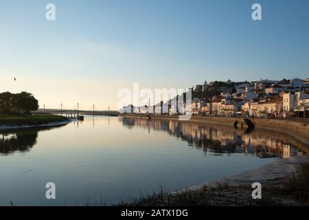 Vue sur le paysage urbain d'Alcacer do Sal depuis l'autre côté de la rivière Sado au coucher du soleil Banque D'Images