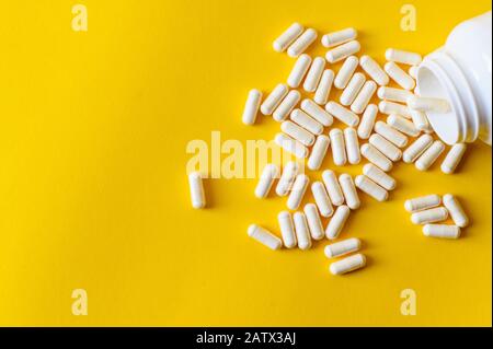 Groupe de comprimés blancs assortis. Capsules qui débordent de la bouteille jaune. Fond rouge. Concept de parcours. Banque D'Images