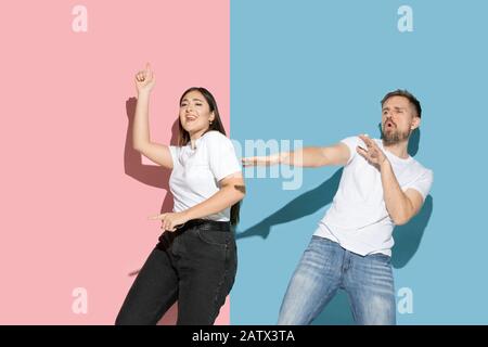 Inspiré. Danser, bouger, s'amuser. Jeune et heureuse homme et femme dans des vêtements décontractés sur fond rose, bleu bicolore. Concept des émotions humaines, de l'expulsion faciale, des relations, de l'annonce. Beau couple. Banque D'Images