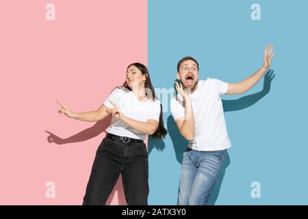 Inspiré. Danser, bouger, s'amuser. Jeune et heureuse homme et femme dans des vêtements décontractés sur fond rose, bleu bicolore. Concept des émotions humaines, de l'expulsion faciale, des relations, de l'annonce. Beau couple. Banque D'Images