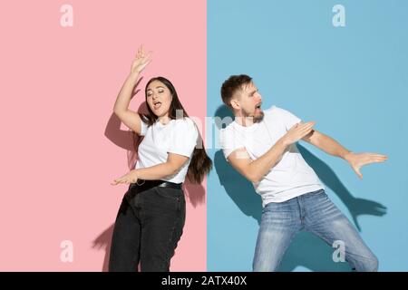 Inspiré. Danser, bouger, s'amuser. Jeune et heureuse homme et femme dans des vêtements décontractés sur fond rose, bleu bicolore. Concept des émotions humaines, de l'expulsion faciale, des relations, de l'annonce. Beau couple. Banque D'Images