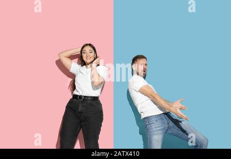 Inspiré. Danser, bouger, s'amuser. Jeune et heureuse homme et femme dans des vêtements décontractés sur fond rose, bleu bicolore. Concept des émotions humaines, de l'expulsion faciale, des relations, de l'annonce. Beau couple. Banque D'Images