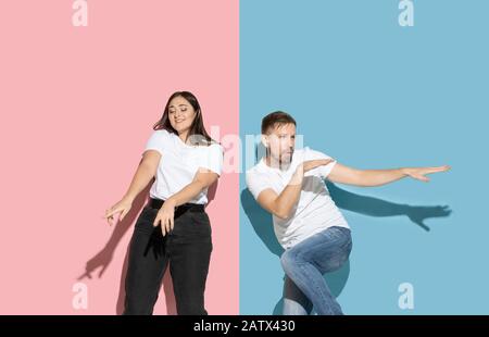 Inspiré. Danser, bouger, s'amuser. Jeune et heureuse homme et femme dans des vêtements décontractés sur fond rose, bleu bicolore. Concept des émotions humaines, de l'expulsion faciale, des relations, de l'annonce. Beau couple. Banque D'Images