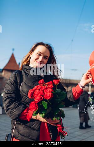 Cadeaux de Saint Valentin. Femme tenant bouquet de roses rouges fleurs et ballons sur la rue de la ville. Bonne amie Banque D'Images