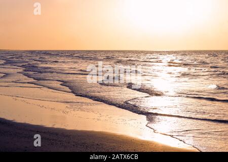 Lever du soleil sur la plage. Des vagues douces frappent le rivage lorsque le soleil s'élève au-dessus de la mer. Voyage et tourisme paysage arrière-plan avec espace de copie. Banque D'Images