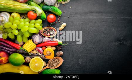Une grande sélection de légumes crus, de fruits et d'épices sur une surface en bois noir. Espace libre pour votre texte. Vue de dessus. Banque D'Images