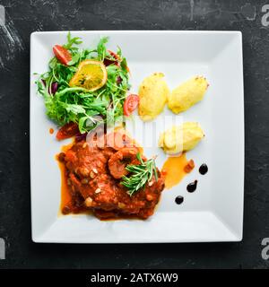 Steak cuit sur l'os avec sauce tomate et pommes de terre dans une assiette. Vue de dessus. Espace libre pour votre texte. Banque D'Images